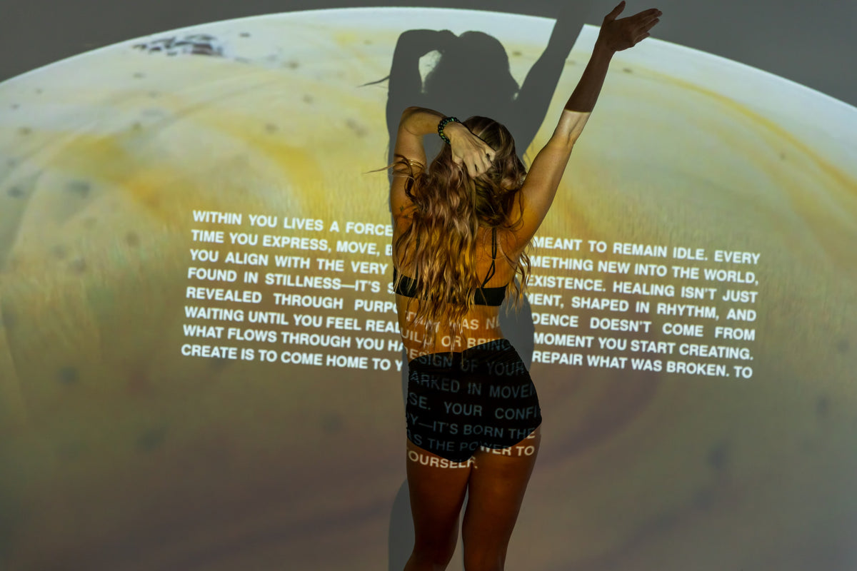 A BUTI practitioner raises her arms in expressive movement under projected words